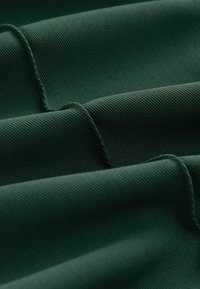 Tissu côtelé vert foncé plié en vagues parallèles douces mettant en valeur la texture et les détails des coutures.