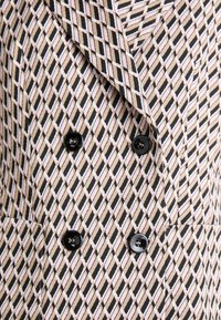 Beige, schwarz-weißes, karriertes Doppelreiher-Blazer. Mit schwarzen Knöpfen und einem Reverskragen, sowie seitlichen Taschen.