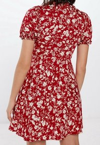 Rotes Blumenkleid mit kurzen Puffärmeln, tailliertem Schnitt und ausgestelltem Rock. Blumenmuster in Weiß auf einem lebendigen roten Hintergrund.