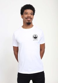 T-shirt bianca a maniche corte in cotone con un logo nero stampato sul petto che presenta un design circolare e il testo: "PILOTI CERCASI."