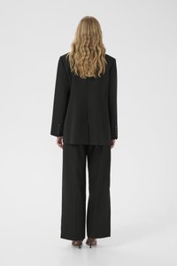 Fekete, testre szabott öltöny, amely egy strukturált blézert és bő szárú nadrágot foglal magában, sima anyagból és gombos részletekkel. Hátulnézet látható.