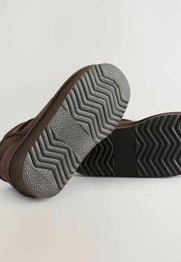 Braune Wildlederstiefel mit strukturierten Gummisohlen, die ein Zickzack-Profilmuster für guten Halt und weiche, abgerundete Kanten aufweisen.