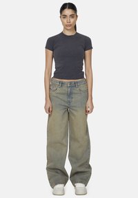 Szara dopasowana koszulka, wysokie jasnoniebieskie szerokie dżinsy i białe trampki. Dżinsy mają wyblakłą fakturę i subtelne detale przeszyć.