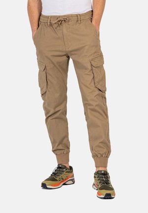 Pantalones cargo color caqui con cintura elástica, cordón ajustable y puños entallados. Presenta dos bolsillos laterales y dos bolsillos en las piernas. Llevados con zapatillas.