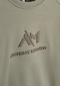 Sudadera verde oliva con cuello redondo y mangas raglán. Presenta un logo bordado en marrón en relieve con el texto "ANTONY MORATO". Textura suave.