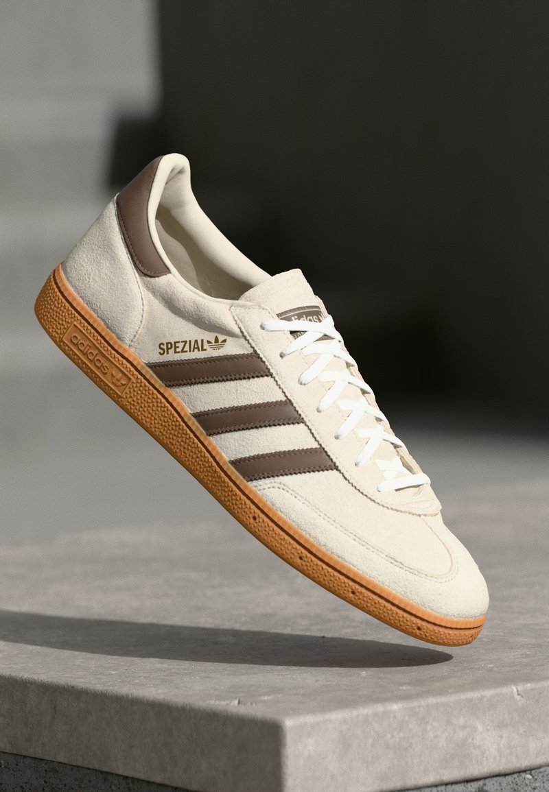 Sneaker bianca in suede con dettagli in pelle marrone, tre strisce marroni e lacci bianchi. Presenta una suola in gomma testurizzata e il logo dorato "SPEZIAL".