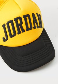 Rumena bejzbolska kapa s črnim vizirjem in embosiranim logotipom "JORDAN". Ima strukturirano zasnovo in teksturirano blago.