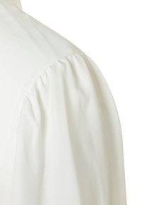 Weiße Bluse mit gepufften Ärmeln und geraffter Textur an der Schulter. Der Stoff hat eine glatte, leicht gerippte Oberfläche.
