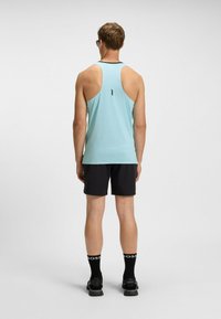 Canottiera senza maniche di colore blu chiaro con design a racerback, abbinata a pantaloni corti neri, logo visibile sui calzini e scarpe sportive.