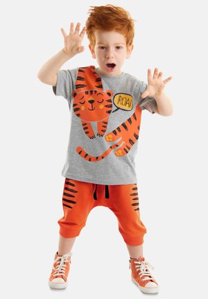 Graues T-Shirt mit kurzen Ärmeln und orangefarbenen Tigergrafiken, kombiniert mit orangen Hosen mit schwarzen Streifen und orangenen Sneakers.