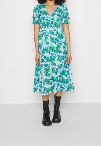 Blommig klänning i blå och gröna nyanser, korta puffärmar, v-ringning och en utsvängd kjol, tillsammans med svarta ankelstövlar.