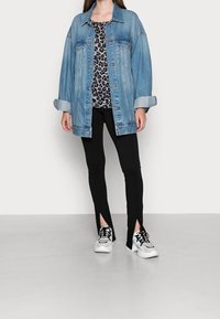 Jeansjacke mit lockerer Passform, blauer Farbe und knöpfbarer Vorderseite, über einem Leopardenmuster-Oberteil getragen. Schwarze enge Hosen mit seitlichen Schlitzen.