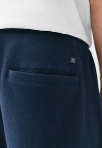 Mornarske hlače teksturirane tkanine s malim srebrnim logom na pojasu i detaljem džepa, izrađene od prozračne tkanine za udobnost.