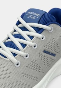 Világosszürke sneaker fehér cipőfűzőkkel, kék hálós nyelvvel és díszítéssel, a nyelven és az oldalon "JACK & JONES" márkázással.