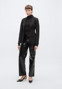 Fekete, testhezálló szabású blézer fekete garbóval, fényes fekete vinil bőszárú nadrággal és fekete slingback magassarkúval kombinálva.