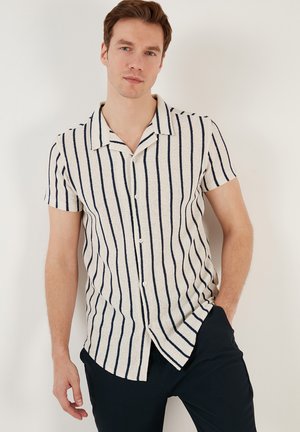 Camisa de manga corta hecha de tejido texturizado en color crema con rayas verticales en azul marino, con cuello en pico y cierre de botones en el frente.