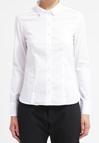 Camicia bianca con colletto a punta, maniche lunghe e vestibilità slim. Realizzata in tessuto liscio con una texture semplice.