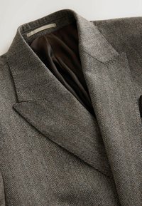 Żakiet w wzór houndstooth w odcieniach szaro-brązowych, z klapami, teksturowaną powierzchnią i brązową podszewką.