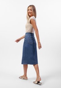 Denim midi-skjørt med høy midje, blå vask og baklommer. Stillet med en tettsittende kremfarget skjorte og metalliske slingback-sandaler.