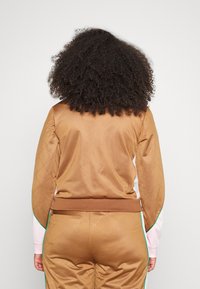 Brown quilted sports jacket with a fitted hem and contrasting mint green accent along the sleeves, featuring a smooth, glossy texture.