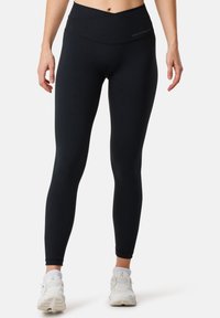 Black leggings with a high waistband, made of stretchy material. Features a seamless design and subtle logo detail near the top.