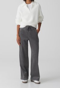 Pantalon en velours côtelé gris avec une taille  élastique à cordon, des poches latérales et une coupe décontractée, associé à un pull blanc duveteux.