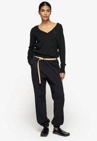 Czarny sweter w kształcie V z długimi rękawami, zestawiony z luźnymi czarnymi spodniami, przewiązany beżowym paskiem. Na swetrze znajduje się prosty logo.