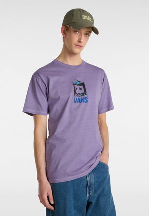 Purple cotton t-shirt with a crew neckline, featuring a graphic design in black and blue. Paired with relaxed denim jeans and a green cap.