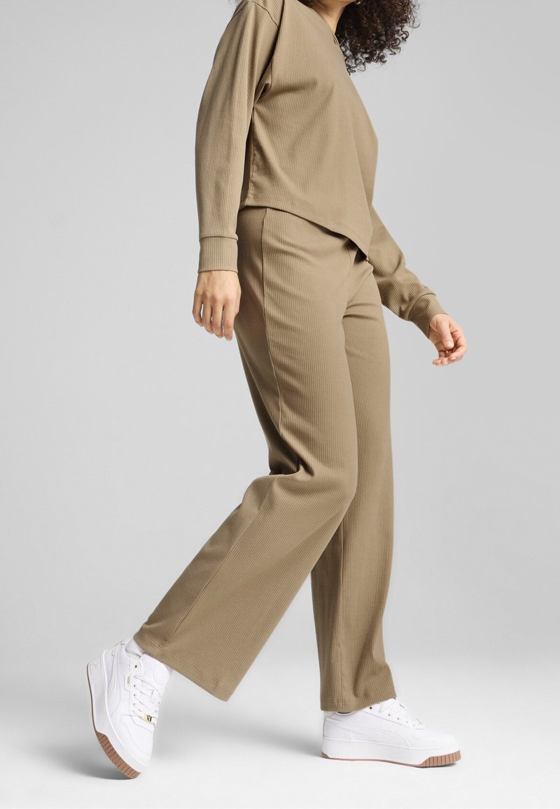 Pull beige côtelé et pantalon large assorti, associés à des baskets blanches, avec un design épuré et une coupe décontractée.