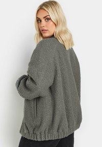 Överdimensionerad, mjuk grå fleecejacka med en strukturerad yta, ribbat nederkant och sidofickor, med en avslappnad passform och voluminösa ärmar.