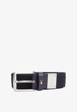 Ceinture en tissu tissé bleu marine avec boucle en métal argenté et petit logo rectangulaire rouge, blanc et bleu sur la boucle en cuir.