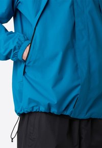 Modrá voděodolná bunda s elastickými manžetami a stahovacím lemem. Obsahuje kapsy na zip a hladký, matný povrch.