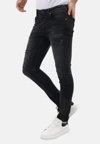 Zwarte skinny jeans met versleten details, voorzien van een klassieke vijfzakkenontwerp en subtiele vervaging, aangevuld met witte sneakers.