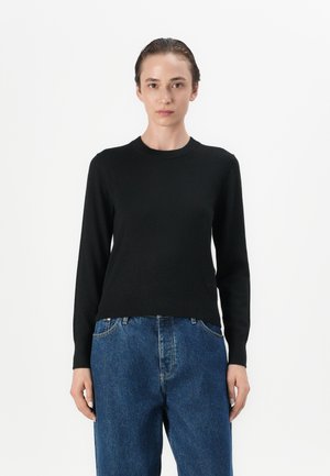 Svart langermet strikkegenser med rund hals, kombinert med løse blå denimjeans. Enkelt design med en glatt tekstur.
