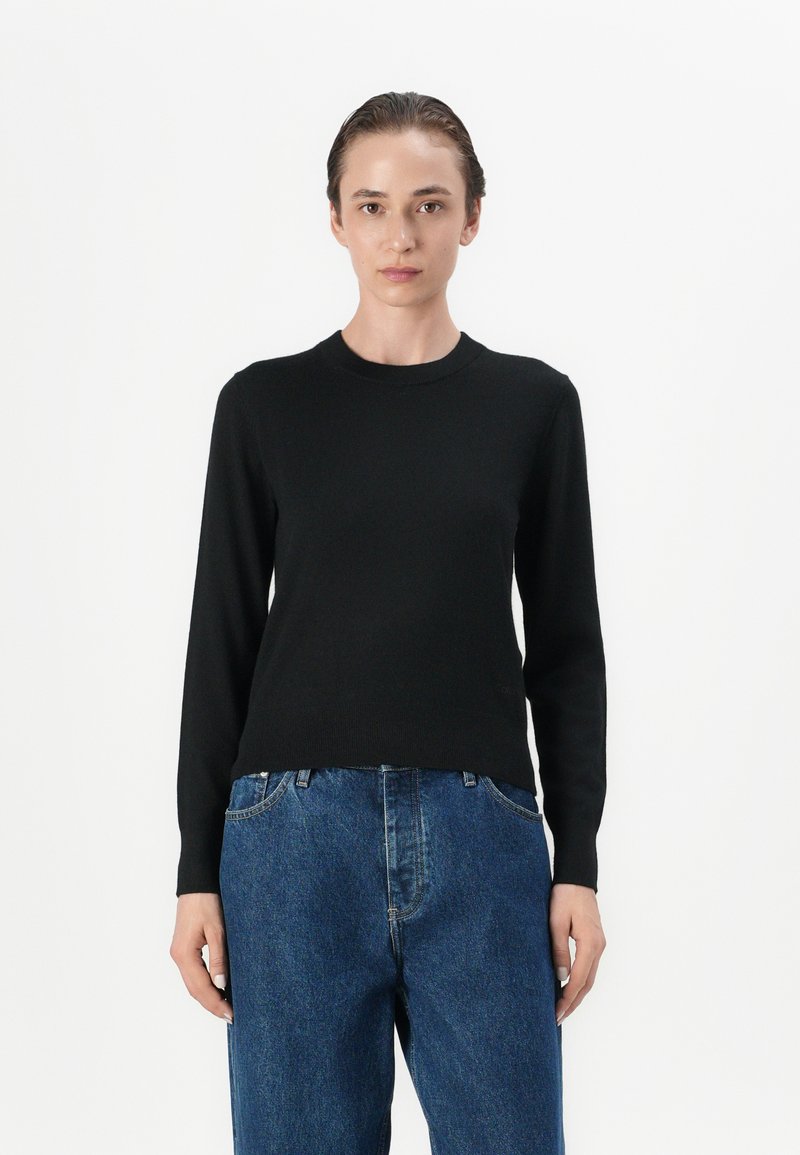 Svart langermet strikkegenser med rund hals, kombinert med løse blå denimjeans. Enkelt design med en glatt tekstur.