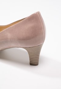 Escarpin nude en cuir verni avec un petit talon empilé et texturé beige sur fond blanc.