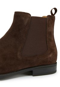 Brown suede ankle boot featuring elastic side panels, a pull tab, and a low rubber heel, showcasing smooth texture and streamlined design.