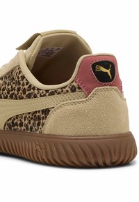 Zapatilla beige con paneles de estampado de leopardo, textura de ante, lengüeta trasera rosa y suela de goma marrón que presenta un pequeño emblema en la parte trasera.