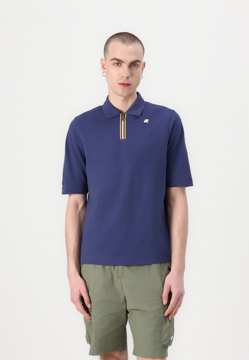Marineblå polo skjorte med detalj i gult og hvitt stripet glidelås, laget av teksturert stoff med korte ermer og en liten logo på brystet.