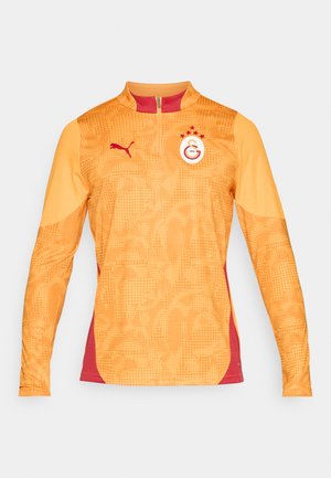 Camisola desportiva laranja de mangas longas com meia abertura, realces vermelhos, padrão texturizado e logótipo com três estrelas e um emblema circular.