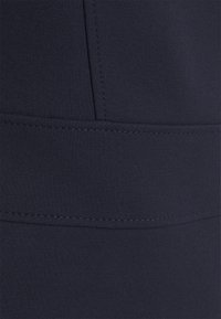 Tmavě modrá látka s hladkou, elastickou strukturou, obsahující horizontální švy a švy pro doplnění designových detailů.