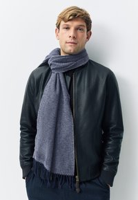 Grauer Fischgrät-Schal mit fransigen Enden, getragen über einer schwarzen Leder-Bomberjacke. Der Schal ist weich und strukturiert und bietet Wärme.