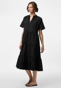 Must mustreening must särk, lühikeste varrukatega, V-kaelusega, mitme kihiga ruffle disainiga, põlvini ulatuv ja nööriga kaela detailiga. Kandmisel mustad sandaalid.