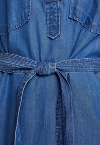 Robe en denim avec une ceinture nouée à la taille et des détails de surpiqûres visibles à l'avant et aux passants de ceinture.