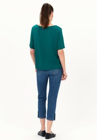 Teal, losse top met korte mouwen en een afgeronde halslijn aan de achterkant, gecombineerd met cropped, licht flare blauwe jeans en zwarte schoenen.