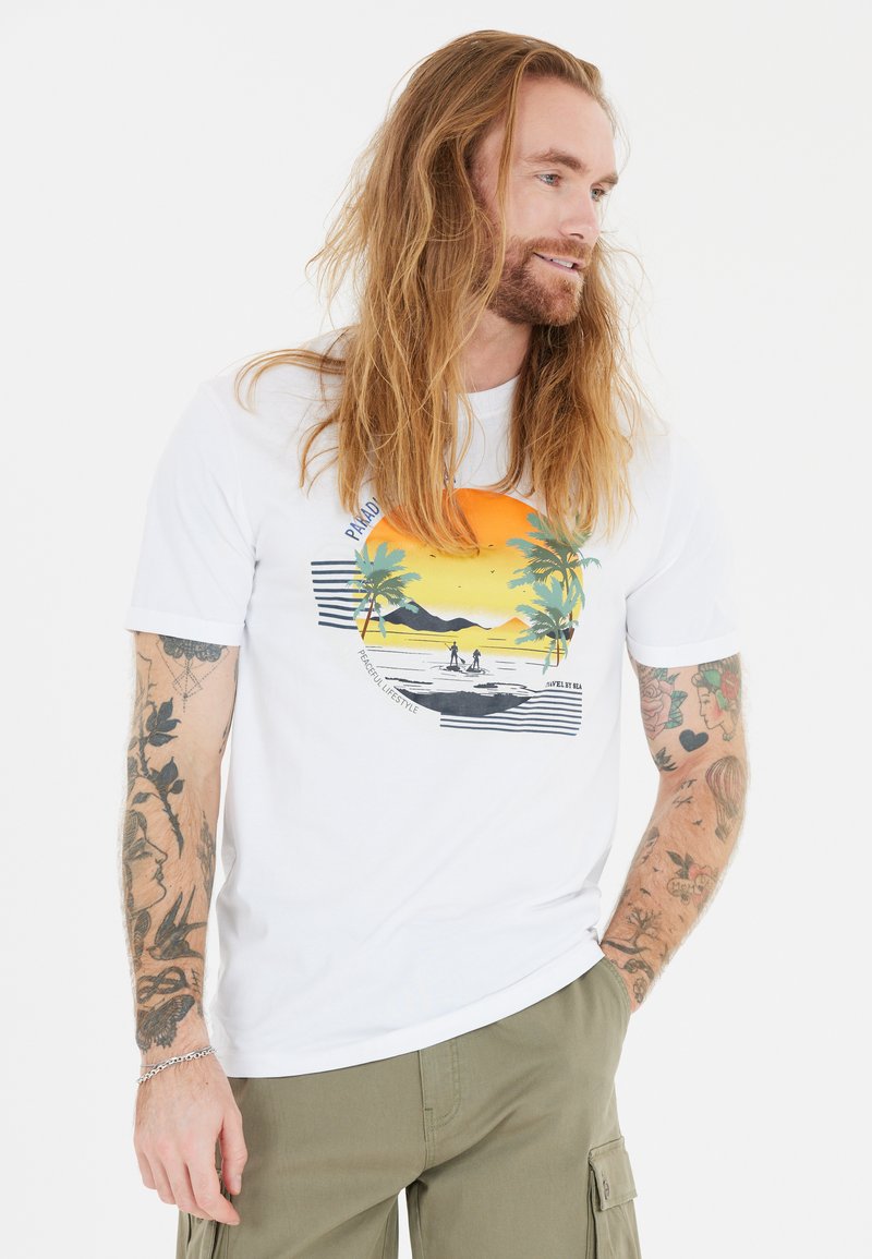 Wit T-shirt met korte mouwen met een kleurrijke zonsondergangafbeelding van palmbomen, bergen en gestreepte accenten. G gecombineerd met olijfkleurige cargo pants.