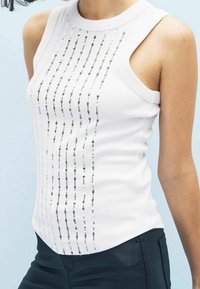 Haut sans manches blanc avec une texture côtelée, présentant des lignes verticales de sequins argentés sur le devant. Encolure ronde, coupe ajustée.