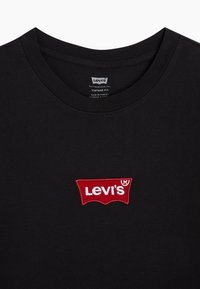 Svart Levi's t-shirt med röd och vit Levi's logotyp patch centrerad under den runda halsringen och synlig varumärkesetikett inuti kragen.