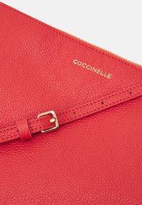 Rød læder clutch med struktureret overflade, gylden lynlås og metal spænde akcent. Logoet er præget i guld på overfladen.