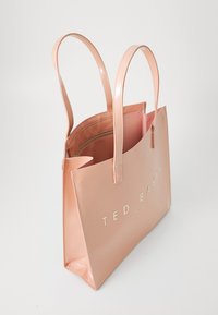 Ružová lesklá taška na rameno s dvoma dlhými uchami, ktorá má na prednej strane zlatý nápis "TED BAKER" a vnútorné vrecko so zipsom.